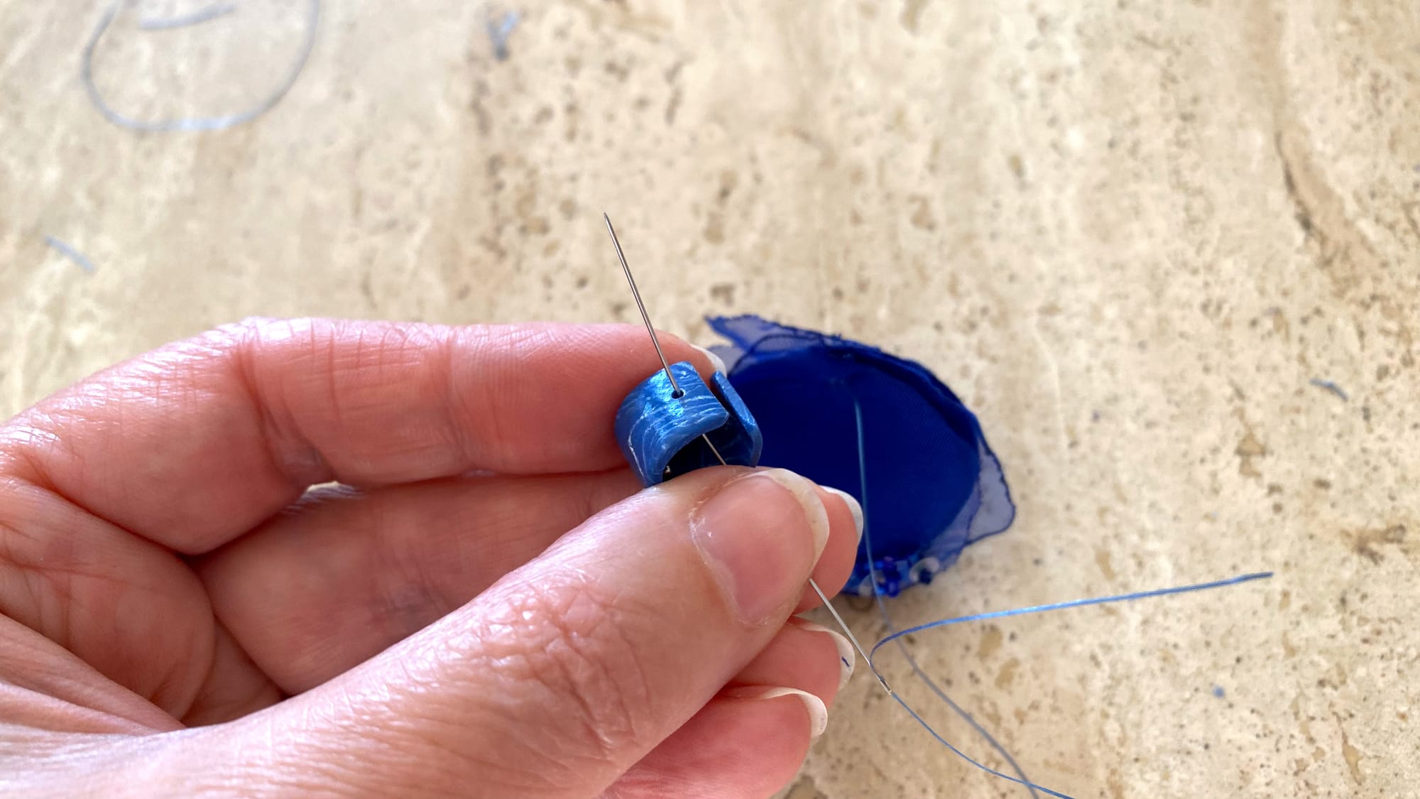 Moving the needle through the hole at the edge of the polymer clay element to connect the fabric part.