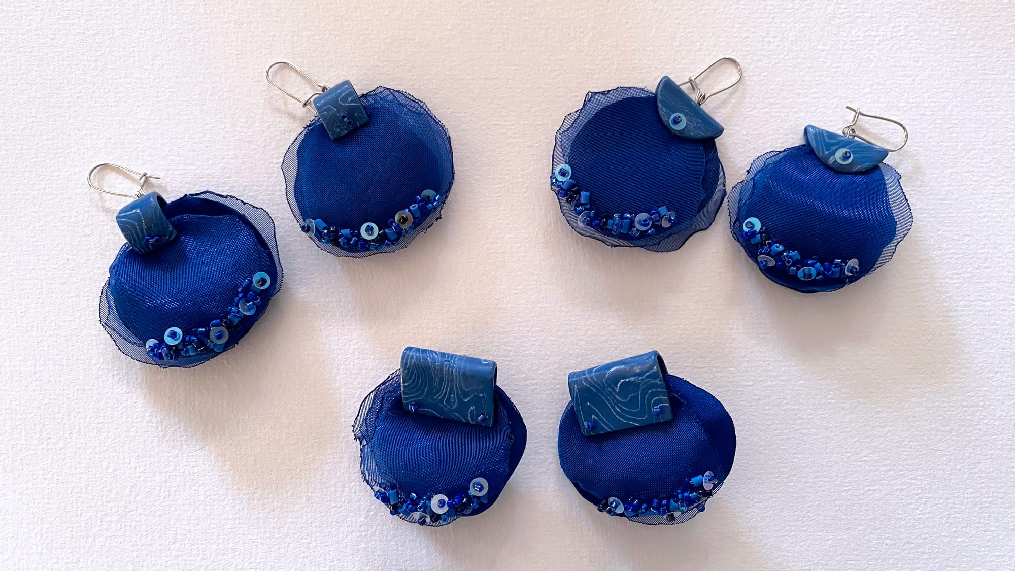 Three pairs of earrings with floral embroidered petals made of organza and polyester fabric, and polymer clay elements.