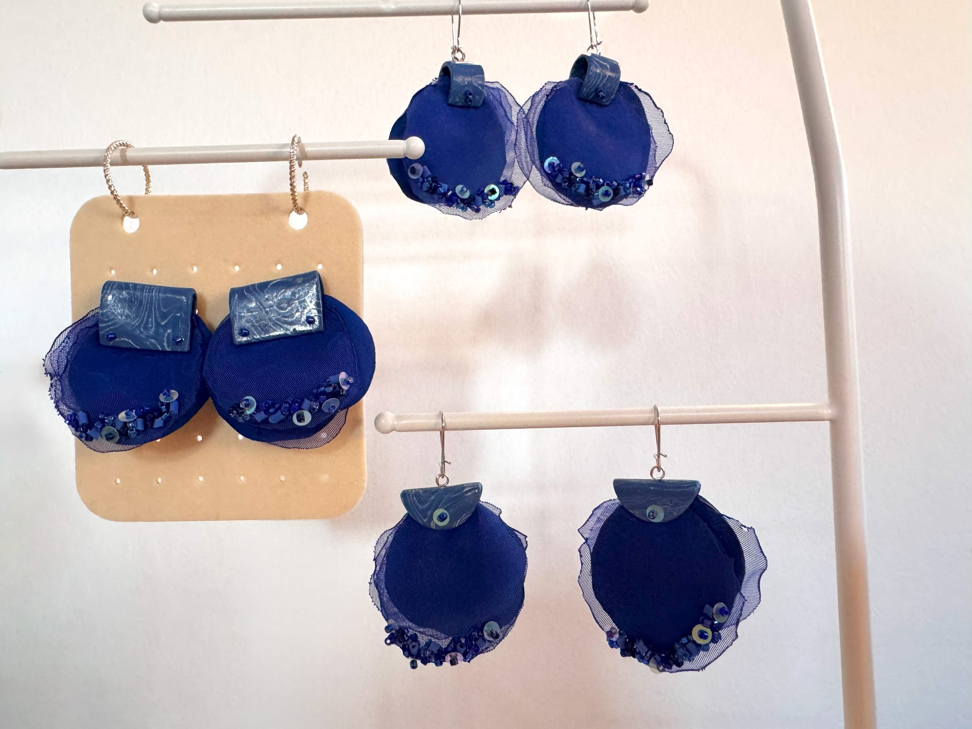 Three pairs of deep blue fabric floral earrings.